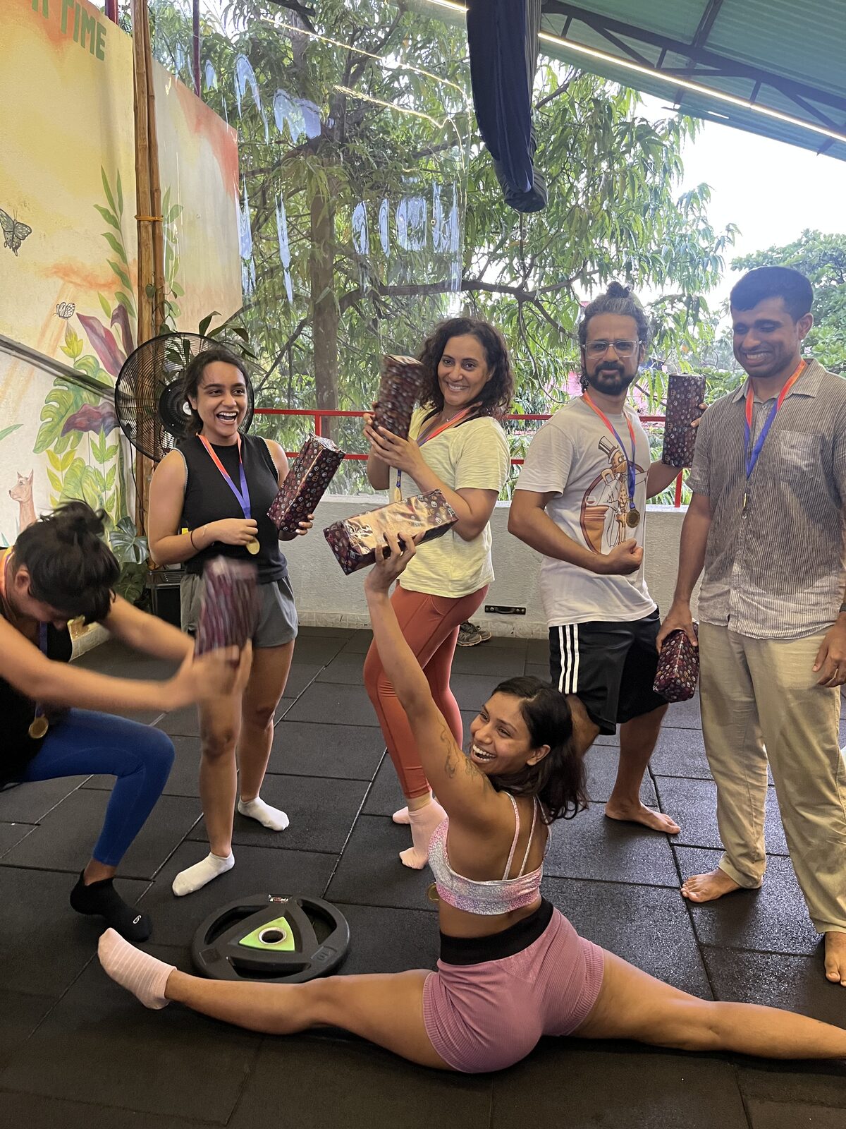 The winning team of The Beginning wearing medals and holding their prizes, one teammate holding a gift up while doing a split
